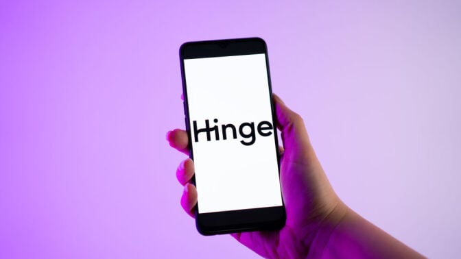 A person holding a mobile phone with the Hinge dating app logo on its screen.