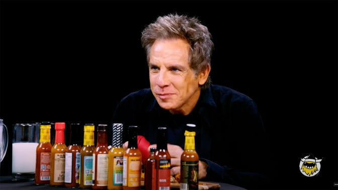 A man sits at a table covered in hot sauce in a dark room.