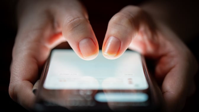 Close-up of two thumbs touching on a smartphone screen in the dark.