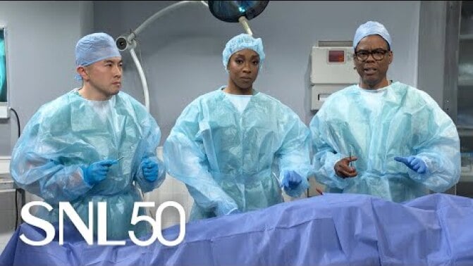 Chris Rock and SNL cast members Bowen Yang and Ego Nwodim dressed as surgeons at an operating table. 