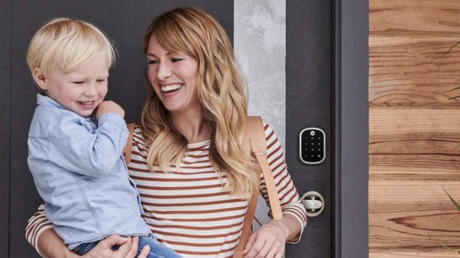 woman holding small child next to a smart lock outside their front door