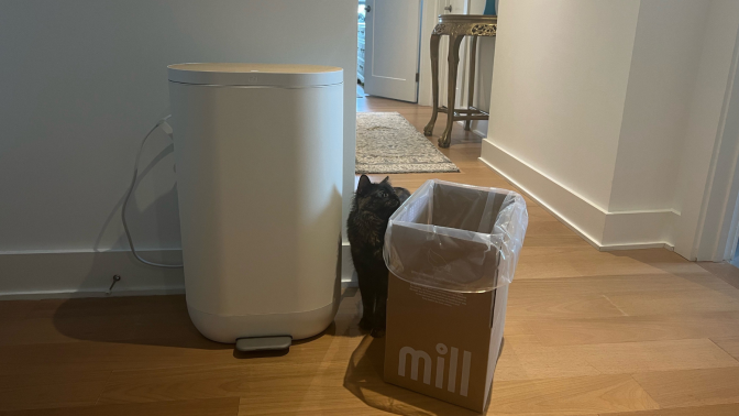 Mill composter bin, cardboard box, and cat with hallway and table in background