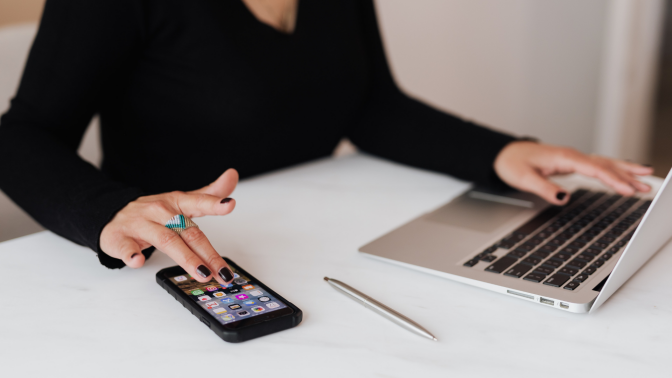 Woman using smartphone while on her laptop 