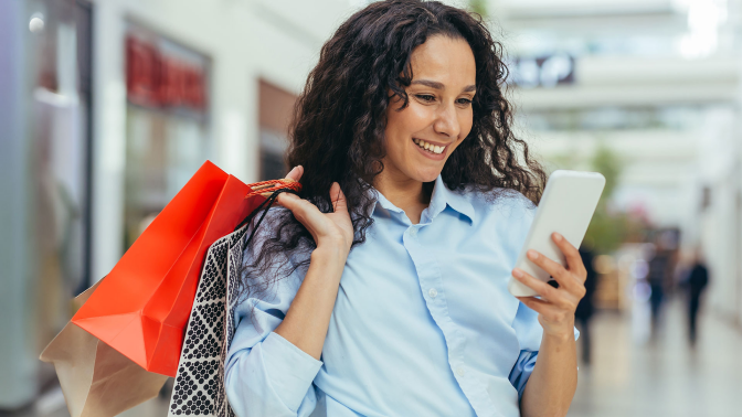 Woman in mall looking at her mobile phone while holding shopping bags